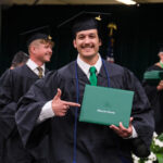 Student smiling and pointing to their degree