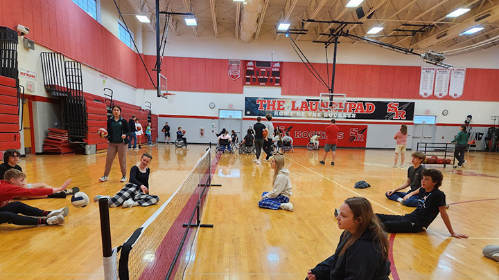 Seated volleyball game in the foreground and a wheelchair basketball game in the background.