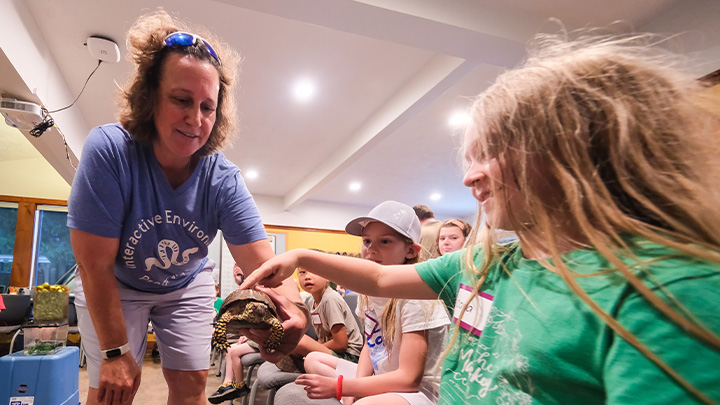 April Claus holds a turtle while the child pets it.
