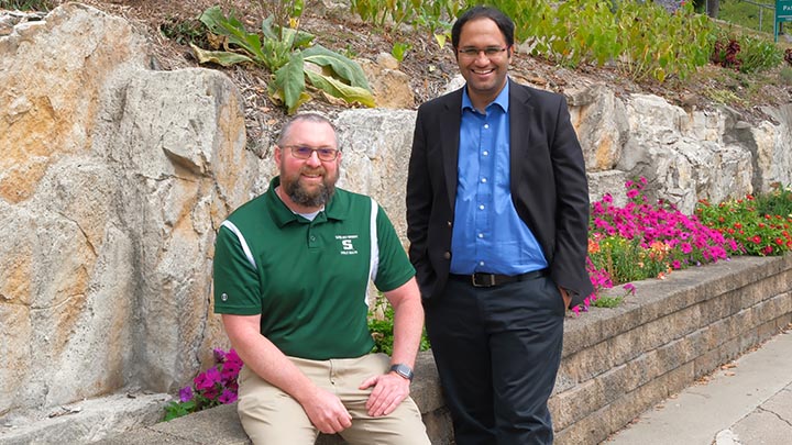 Two professors, one sitting on a wall and one standing.