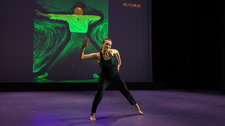 Dancer on stage in front of visual art on screen behind her.