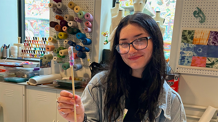 Alexa Rivero holding a stick with yarn in an art studio.