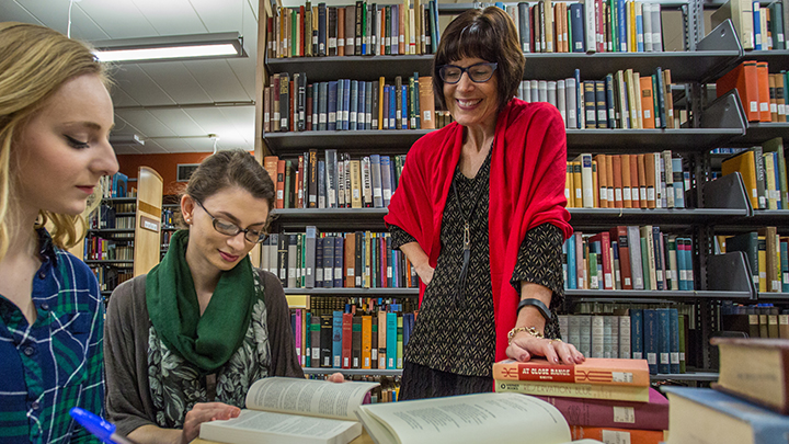 Danette DiMarco standing over two students in the library teaching.