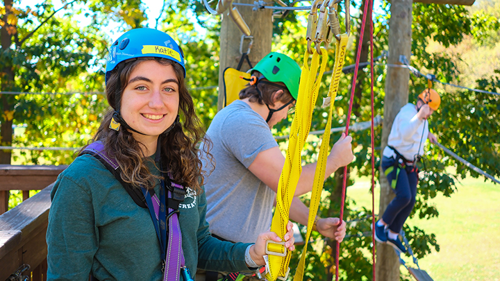Katie Weiner wearing a helmet holding ropes near two students on the ropes course.