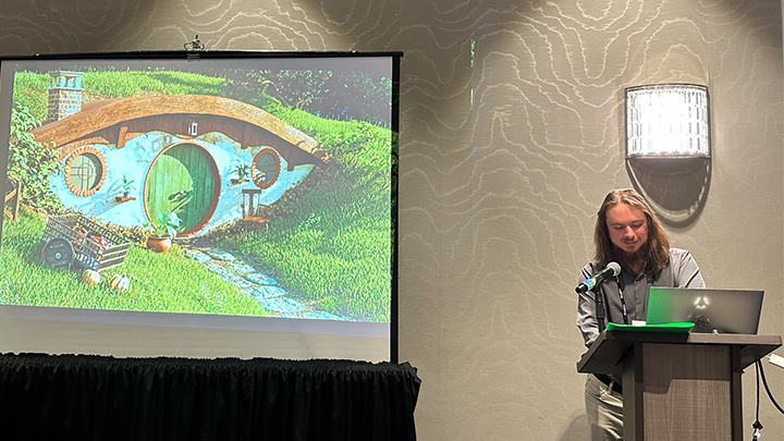 Presenter at podium next to a slide from The Hobbit.