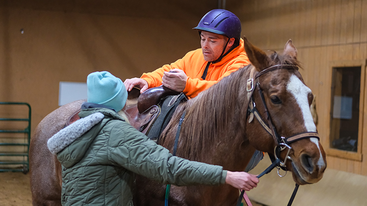 Courtney Gramlich, manager of SRU’s Storm Harbor Equestrian Center, assists veteran Ryan Fusco during a therapeutic riding session at the center.