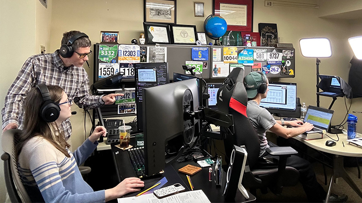 Professor instructing two students sitting in a room in front of monitors.
