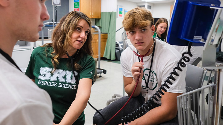 High school student wearing a stethoscope working with a professor