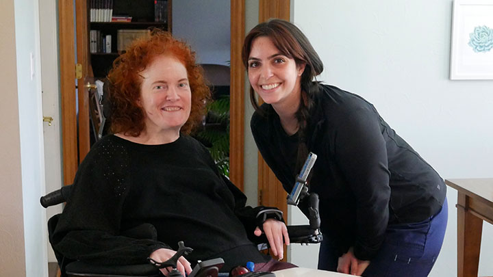 Women using a wheelchair and smart tech device with an occupational therapist.