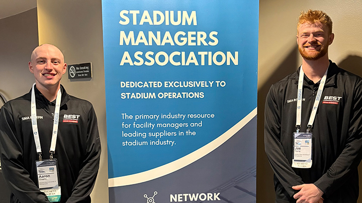 Two students standing next to Stadium Managers Association sign