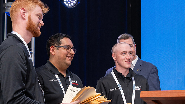 Three students standing on a stage smiling.