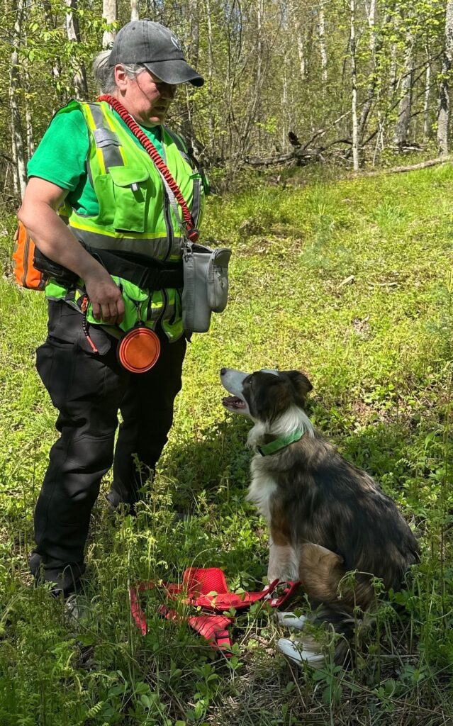 Women with search and rescue tools standing next to dog in woods.