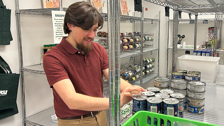 Person stocking shelves with canned goods in a pantry.