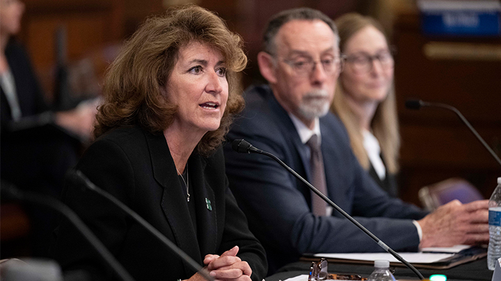 SRU President Karen Riley seated and speaking with two panelists in the background.