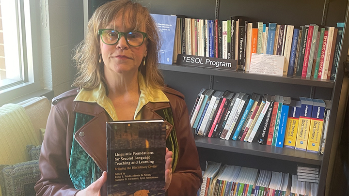 Woman holding a book near a book shelf.
