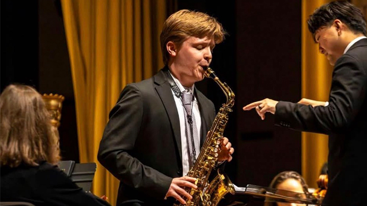 Man playing saxophone on stage with conductor.