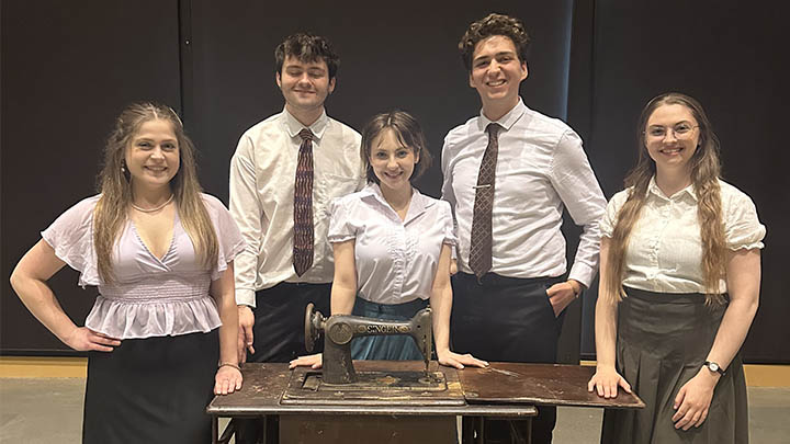 Five theatre cast members standing near a sewing machine.