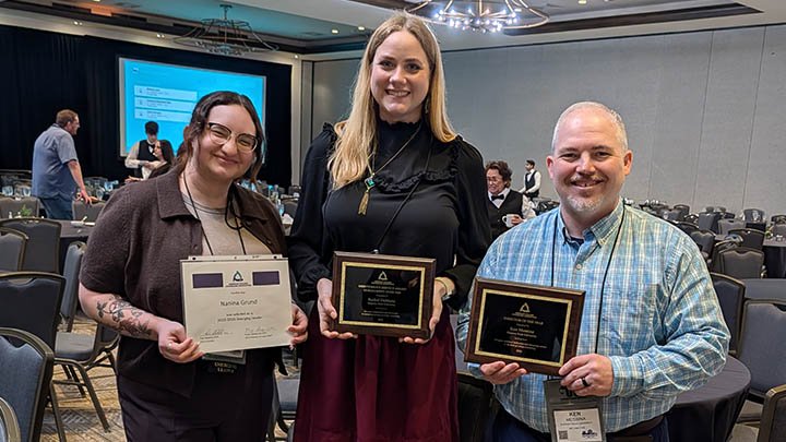 Three people holding awards plaques in a conference hall.