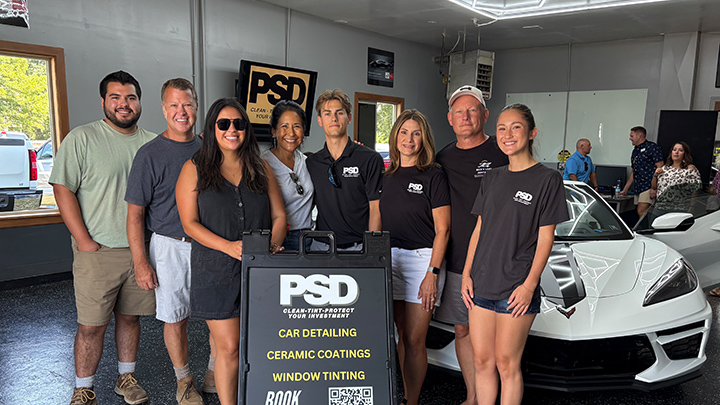 Group of people standing next to a sign and a car. Sign says Prestige Shine Detailing