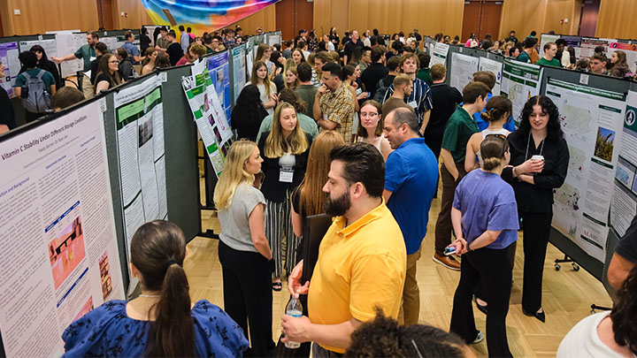 Conference hall with several students presenting their posters to passersby.