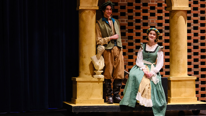Two actors standing on a stage in costume between two pillars.