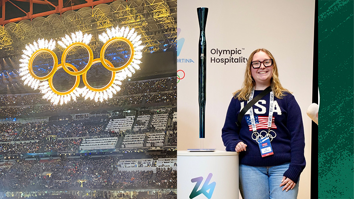 Olympic rings in stadium next to woman standing by Olympic torch.
