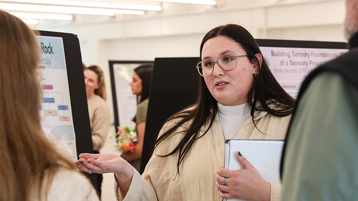 Woman holding a binder talking at a poster presentation event.