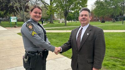 Trooper shaking hands with professor in campus quad.