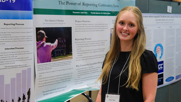Student stands in front of poster presentation.