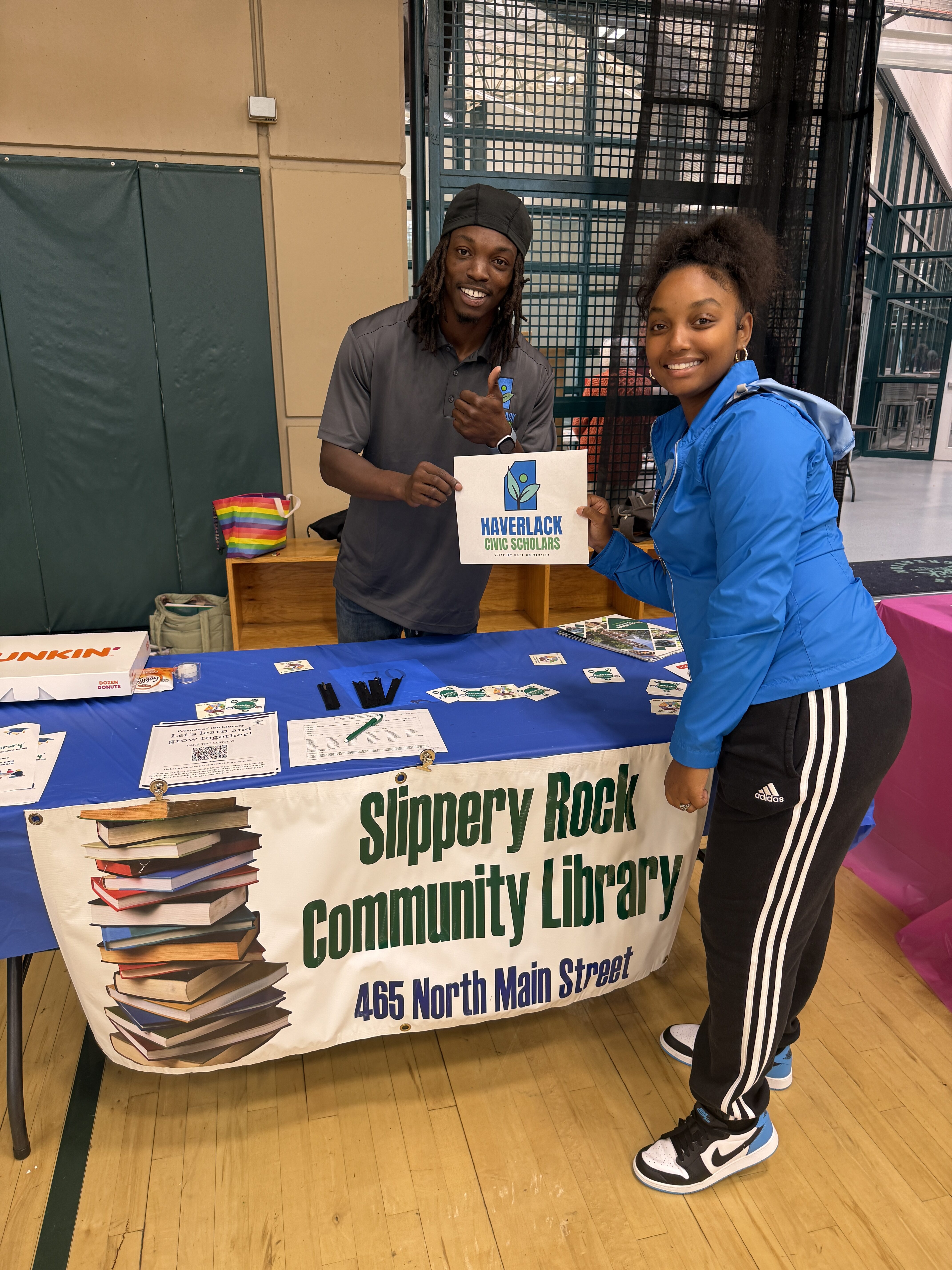 Justin holds a Haverlack Civic Scholars sign with another student at an information table for the Slippery Rock Community Library.