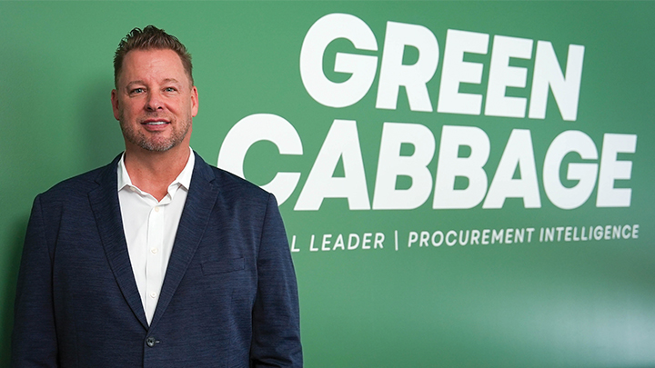 Man in white shirt and blue blazer standing in front of Green Cabbage sign on wall.
