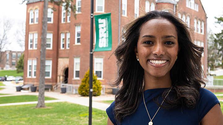 Smiling woman standing in front of SRU banner and Old Main.
