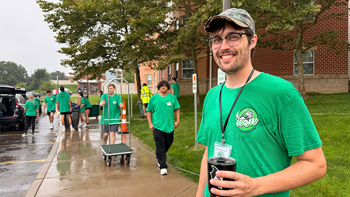 Faculty volunteer standing outside residence hall with movers in background.