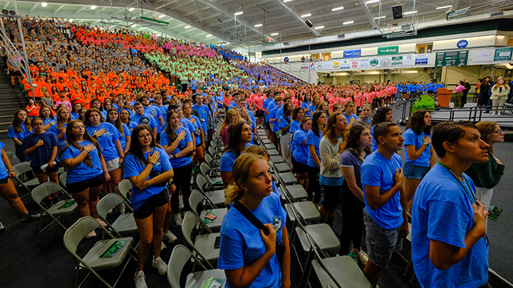 Gymnasium filled with students wearing fluorescent T-shirts and standing for national anthem.