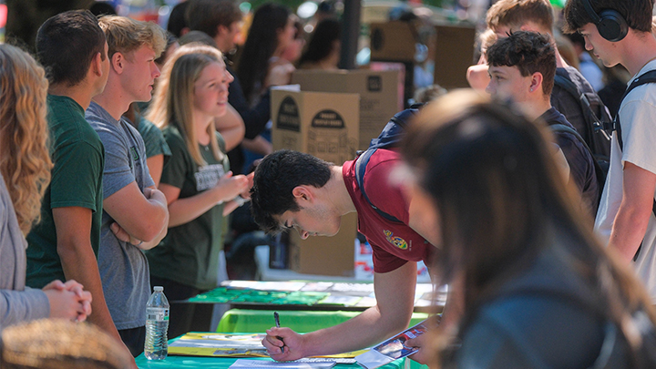 Student signing up for an organization at a table with presenters.