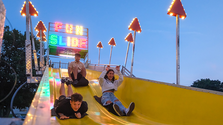 Three students sliding down a fun slide carnival ride.