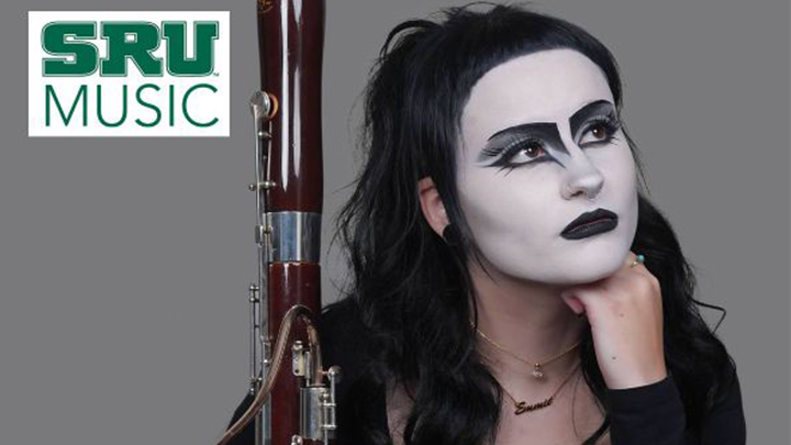 Woman wearing white face paint with hand on chin and holding a bassoon.