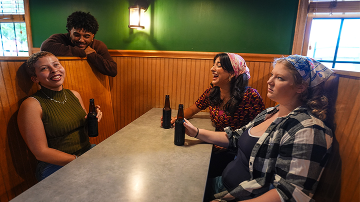 Four people sitting in a booth at a restaurant holding bottles.